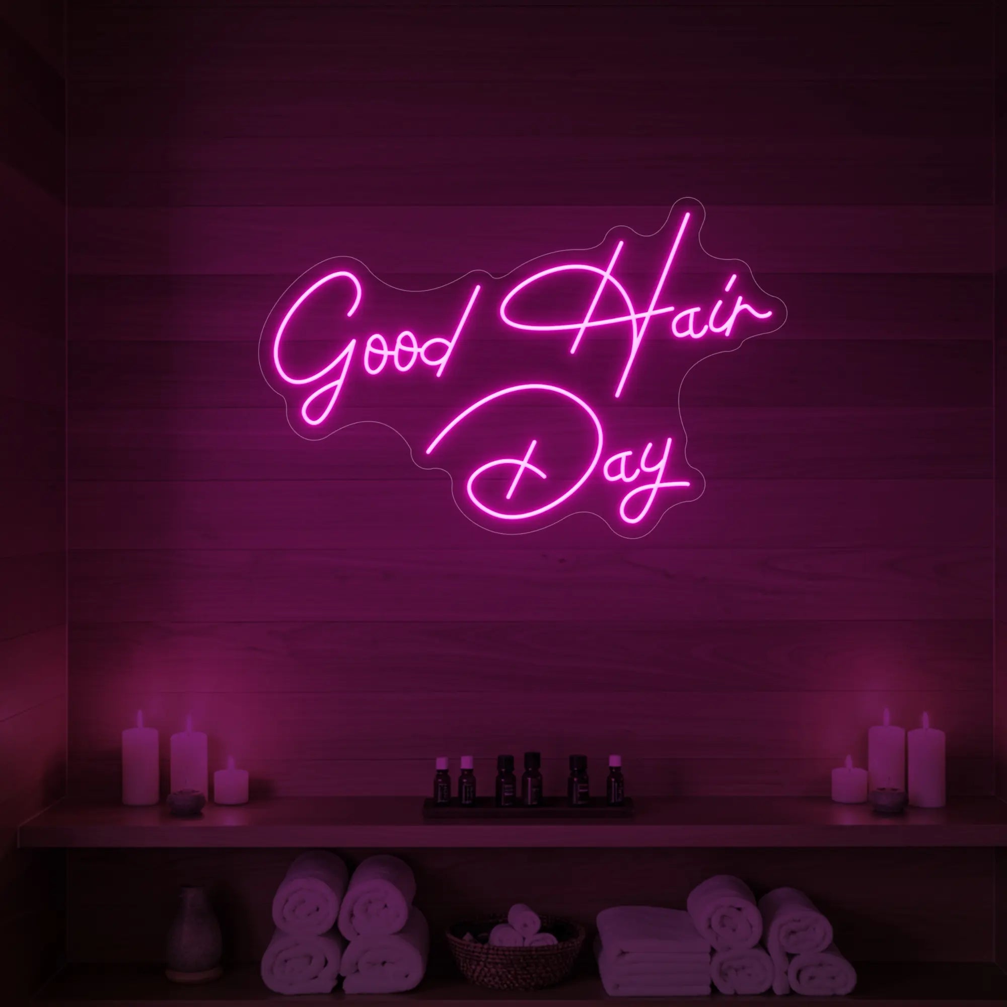 Photo of the 'Good Hair Day' neon sign in cursive glowing in light pink against a styled interior wall.