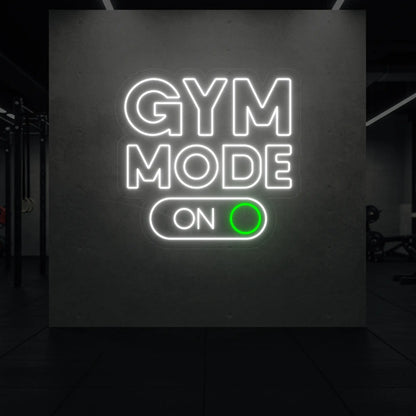 'Gym Mode On' neon sign glowing in cool white and green against a styled interior wall.