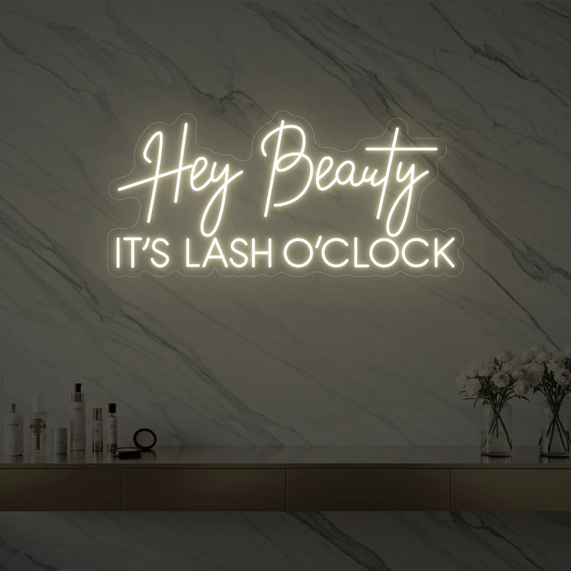 Photo of the 'Hey Beauty IT’S LASH O’CLOCK' neon sign glowing in warm white against a styled interior wall.