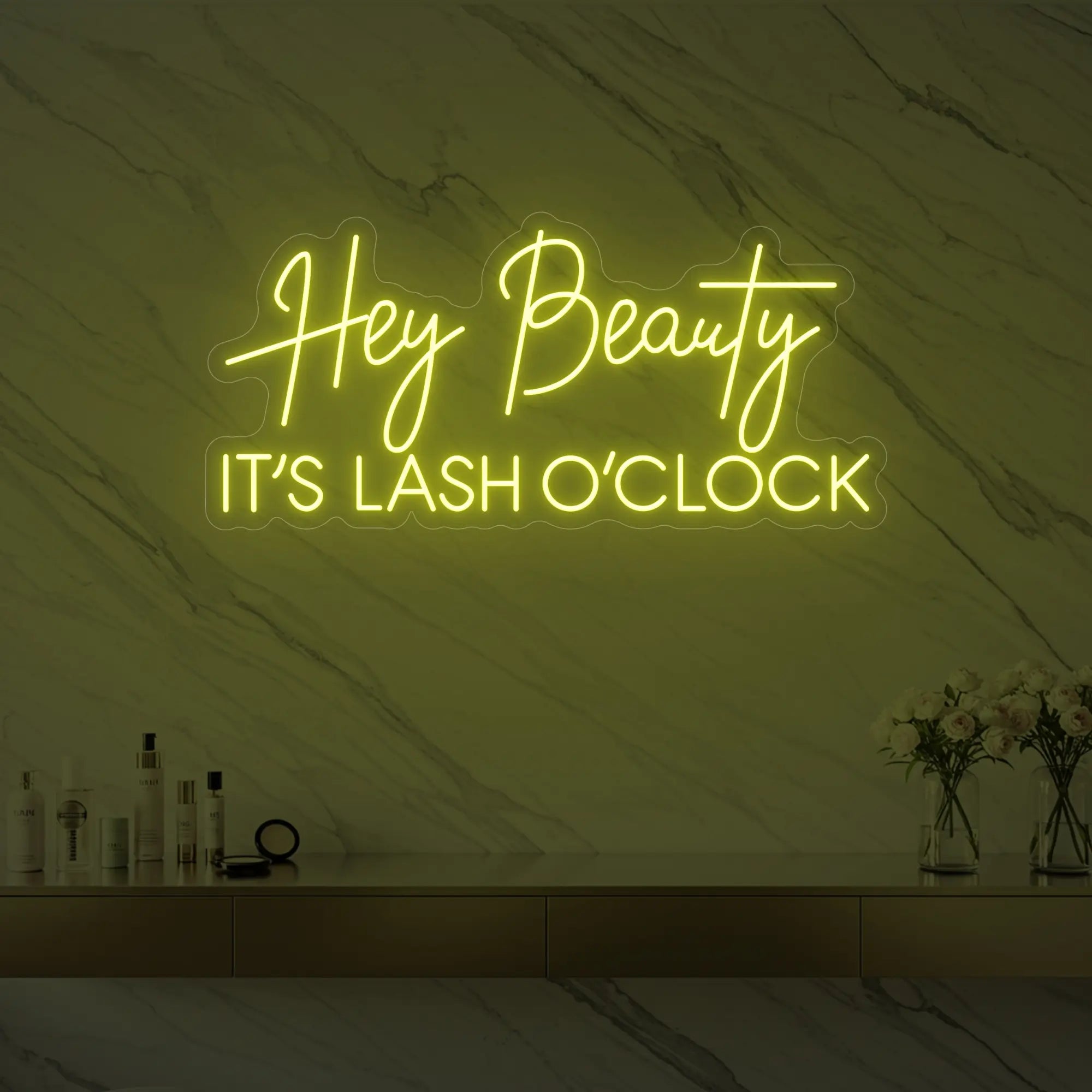 Photo of the 'Hey Beauty IT’S LASH O’CLOCK' neon sign glowing in lemon yellow against a styled interior wall.