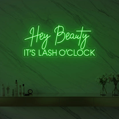 Photo of the 'Hey Beauty IT’S LASH O’CLOCK' neon sign glowing in green against a styled interior wall.