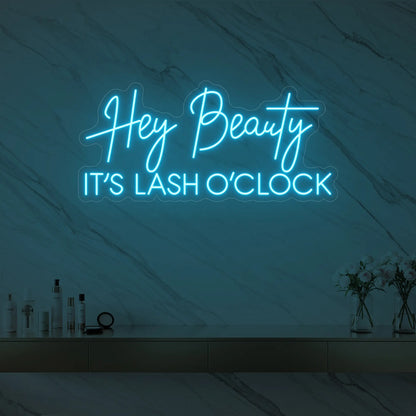 Photo of the 'Hey Beauty IT’S LASH O’CLOCK' neon sign glowing in ice blue against a styled interior wall.