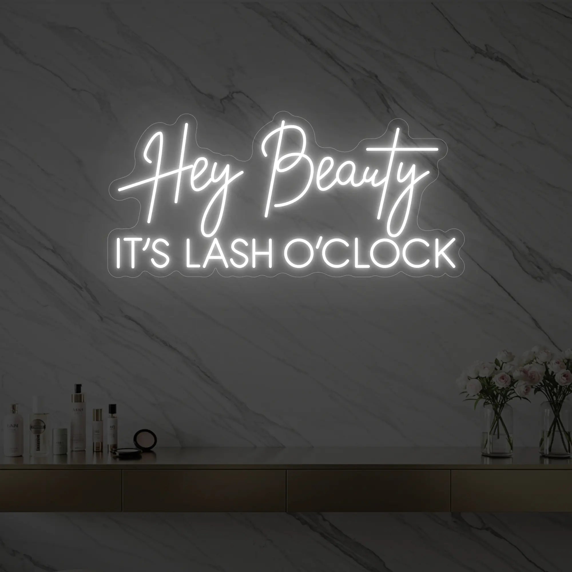 Photo of the 'Hey Beauty IT’S LASH O’CLOCK' neon sign glowing in cool white against a styled interior wall.