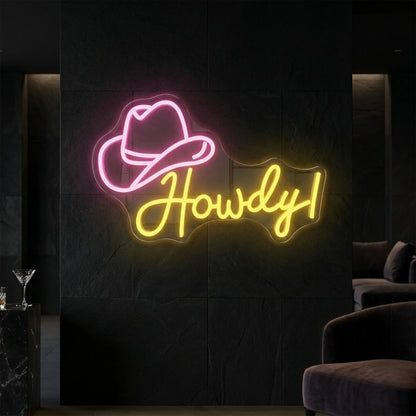 Photo of the 'Howdy!' neon sign glowing in light pink lemon yellow against a styled interior wall.