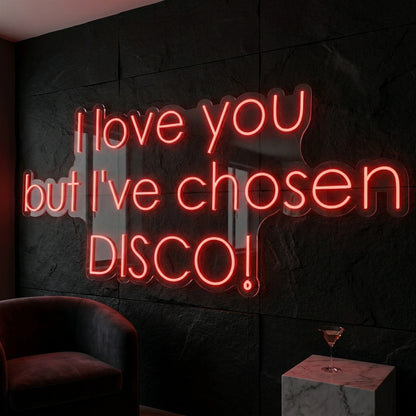 Photo of the 'I Love You But I’ve Chosen Disco' neon sign glowing in red against a styled interior wall.