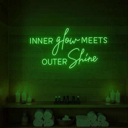 Photo of the 'INNER glow MEETS OUTER Shine' neon sign glowing in green against a styled interior wall.
