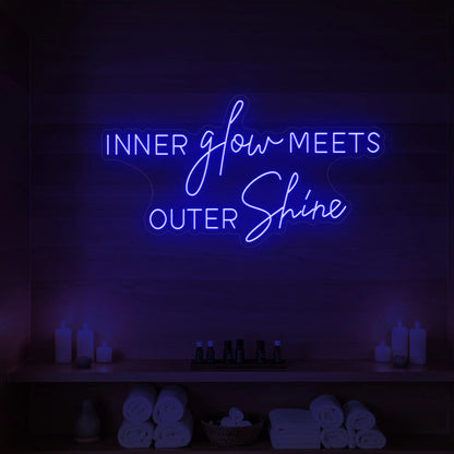 Photo of the 'INNER glow MEETS OUTER Shine' neon sign glowing in deep blue against a styled interior wall.