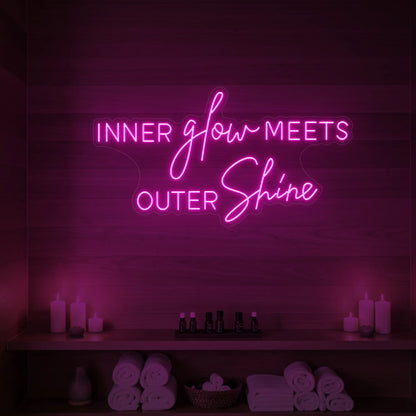 Photo of the 'INNER glow MEETS OUTER Shine' neon sign glowing in light pink against a styled interior wall.