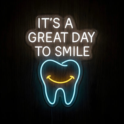 It's a Great Day to Smile LED neon sign featuring glowing white motivational lettering above a blue tooth outline with a yellow smiling face on clear acrylic backing against a dark wooden wall.