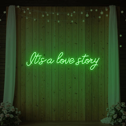 Photo of the 'It’s a Love Story' neon sign glowing in green against a styled interior wall.