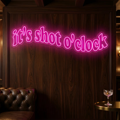 Photo of the 'It’s Shot O’Clock' neon sign glowing in deep pink against a styled interior wall.