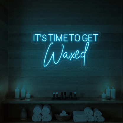 Photo of the 'IT’S TIME TO GET Waxed' neon sign glowing in ice blue against a styled interior wall.