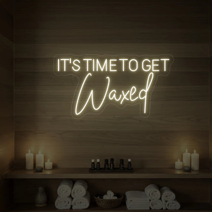 Photo of the 'IT’S TIME TO GET Waxed' neon sign glowing in warm white against a styled interior wall.
