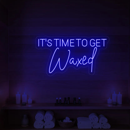 Photo of the 'IT’S TIME TO GET Waxed' neon sign glowing in deep blue against a styled interior wall.