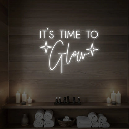 Photo of the 'IT’S TIME TO Glow' neon sign with sparkle icons glowing in cool white against a styled interior wall.