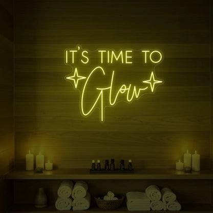 Photo of the 'IT’S TIME TO Glow' neon sign with sparkle icons glowing in lemon yellow against a styled interior wall.