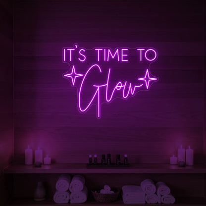 Photo of the 'IT’S TIME TO Glow' neon sign with sparkle icons glowing in deep pink against a styled interior wall.
