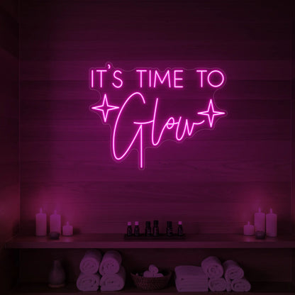 Photo of the 'IT’S TIME TO Glow' neon sign with sparkle icons glowing in light pink against a styled interior wall.