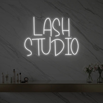 Photo of the 'LASH STUDIO' neon sign glowing in cool white against a styled interior wall.