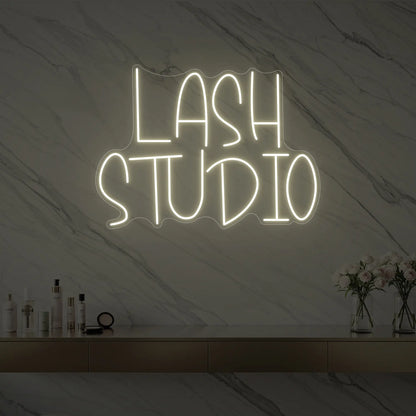 Photo of the 'LASH STUDIO' neon sign glowing in warm white against a styled interior wall.