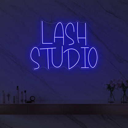 Photo of the 'LASH STUDIO' neon sign glowing in deep blue against a styled interior wall.