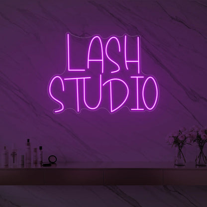 Photo of the 'LASH STUDIO' neon sign glowing in deep pink against a styled interior wall.