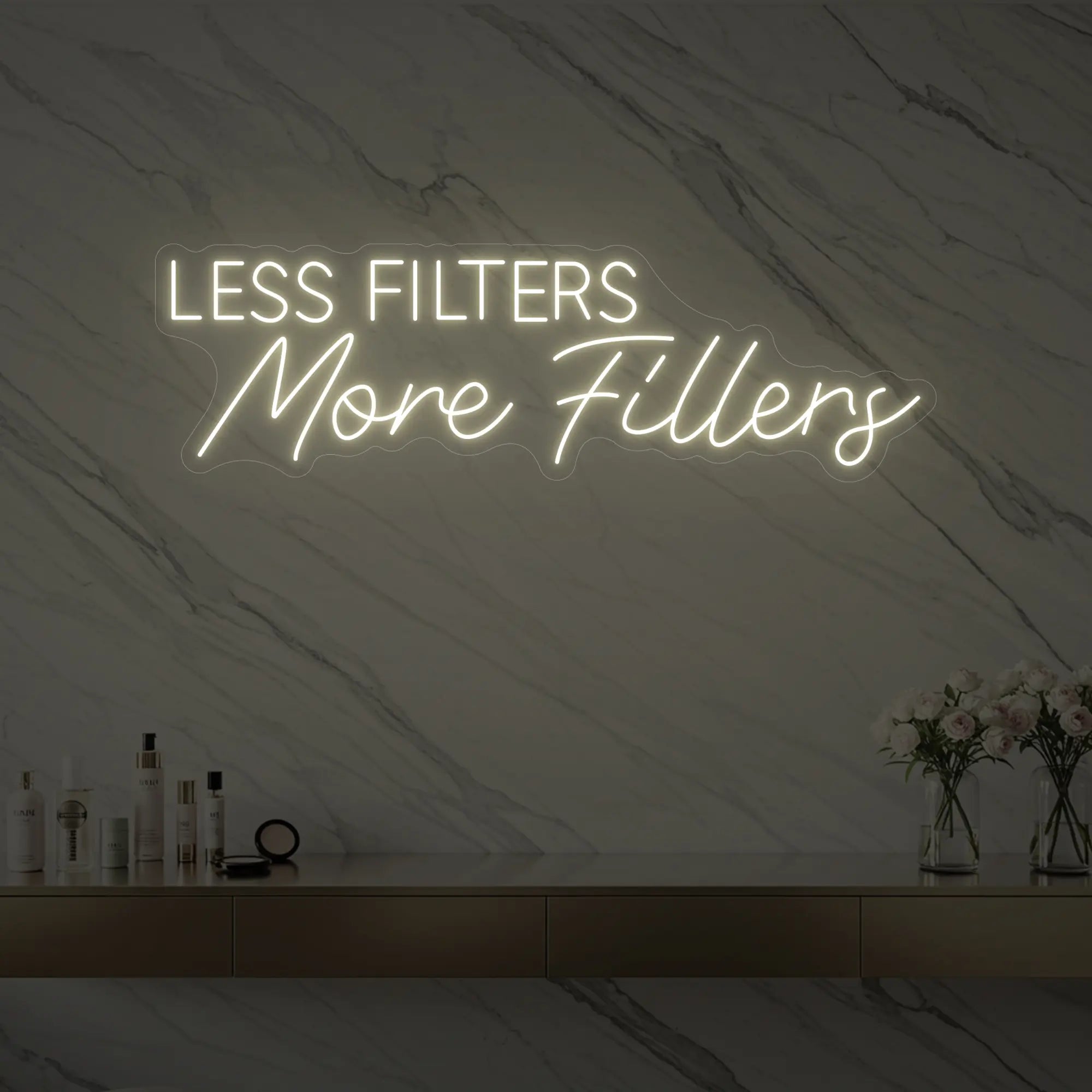 Photo of the 'LESS FILTERS MORE FILLERS' neon sign glowing in warm white against a marble wall.