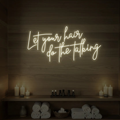 Photo of the 'Let your hair do the talking' neon sign glowing in warm white against a wooden wall.