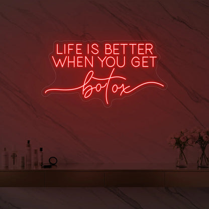 Photo of the 'Life is Better When You Get Botox' neon sign glowing in red against a styled interior wall.