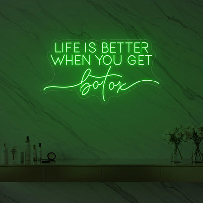 Photo of the 'Life is Better When You Get Botox' neon sign glowing in green against a styled interior wall.
