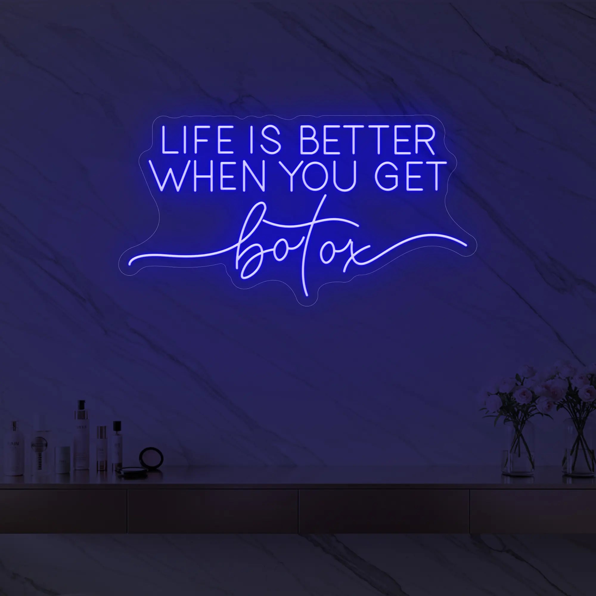 Photo of the 'Life is Better When You Get Botox' neon sign glowing in deep blue against a styled interior wall.