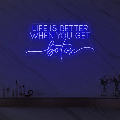 Photo of the 'Life is Better When You Get Botox' neon sign glowing in deep blue against a styled interior wall.