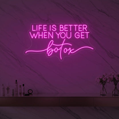 Photo of the 'Life is Better When You Get Botox' neon sign glowing in light pink against a styled interior wall.