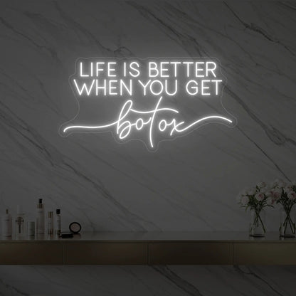 Photo of the 'Life is Better When You Get Botox' neon sign glowing in cool white against a styled interior wall.