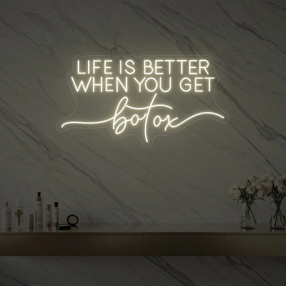 Photo of the 'Life is Better When You Get Botox' neon sign glowing in warm white against a styled interior wall.