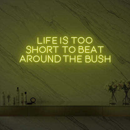 Photo of the 'Life is too short to beat around the bush' neon sign glowing in lemon yellow against a marble wall.