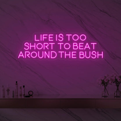 Photo of the 'Life is too short to beat around the bush' neon sign glowing in light pink against a marble wall.