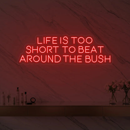 Photo of the 'Life is too short to beat around the bush' neon sign glowing in red against a marble wall.
