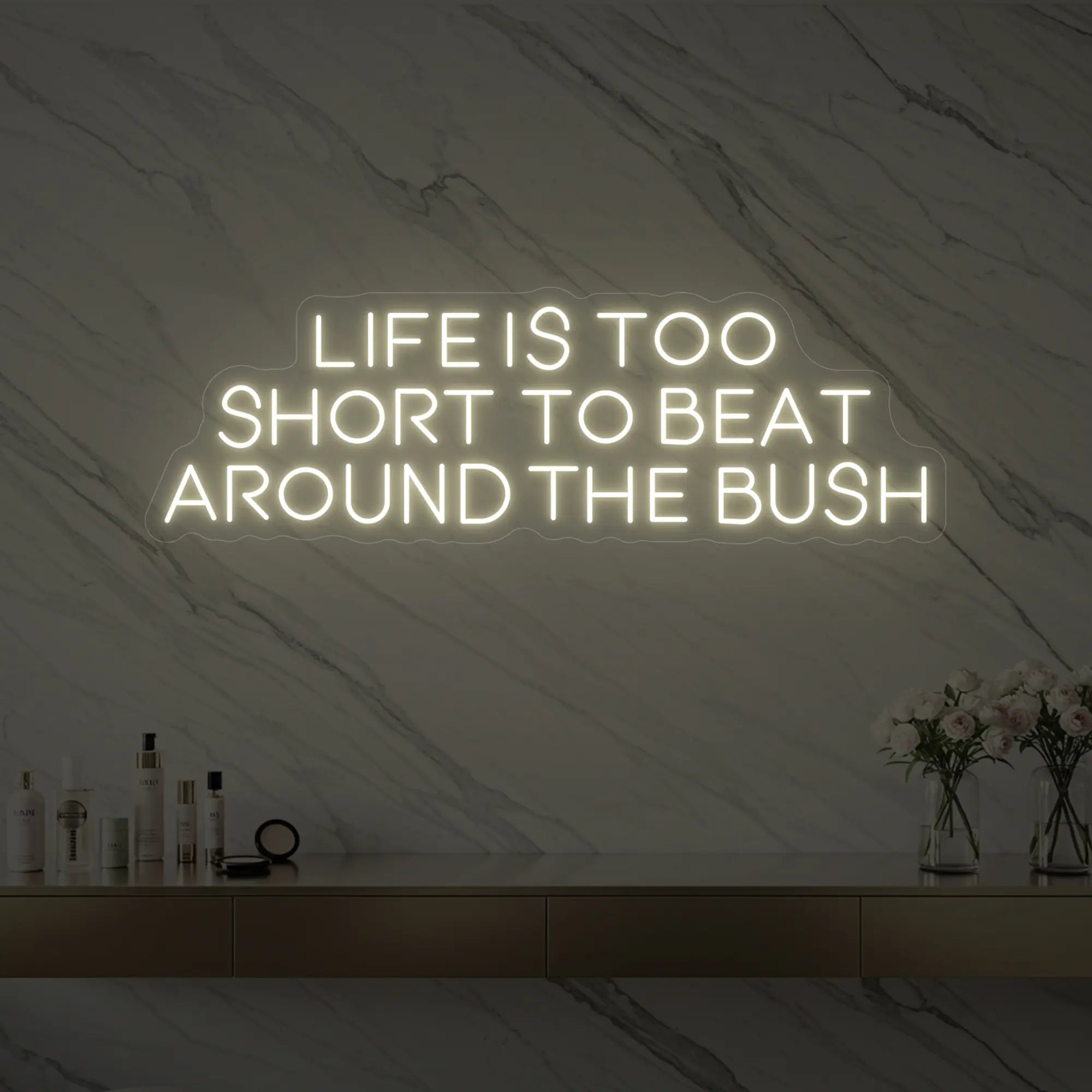 Photo of the 'Life is too short to beat around the bush' neon sign glowing in warm white against a marble wall.