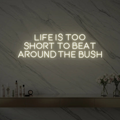 Photo of the 'Life is too short to beat around the bush' neon sign glowing in warm white against a marble wall.