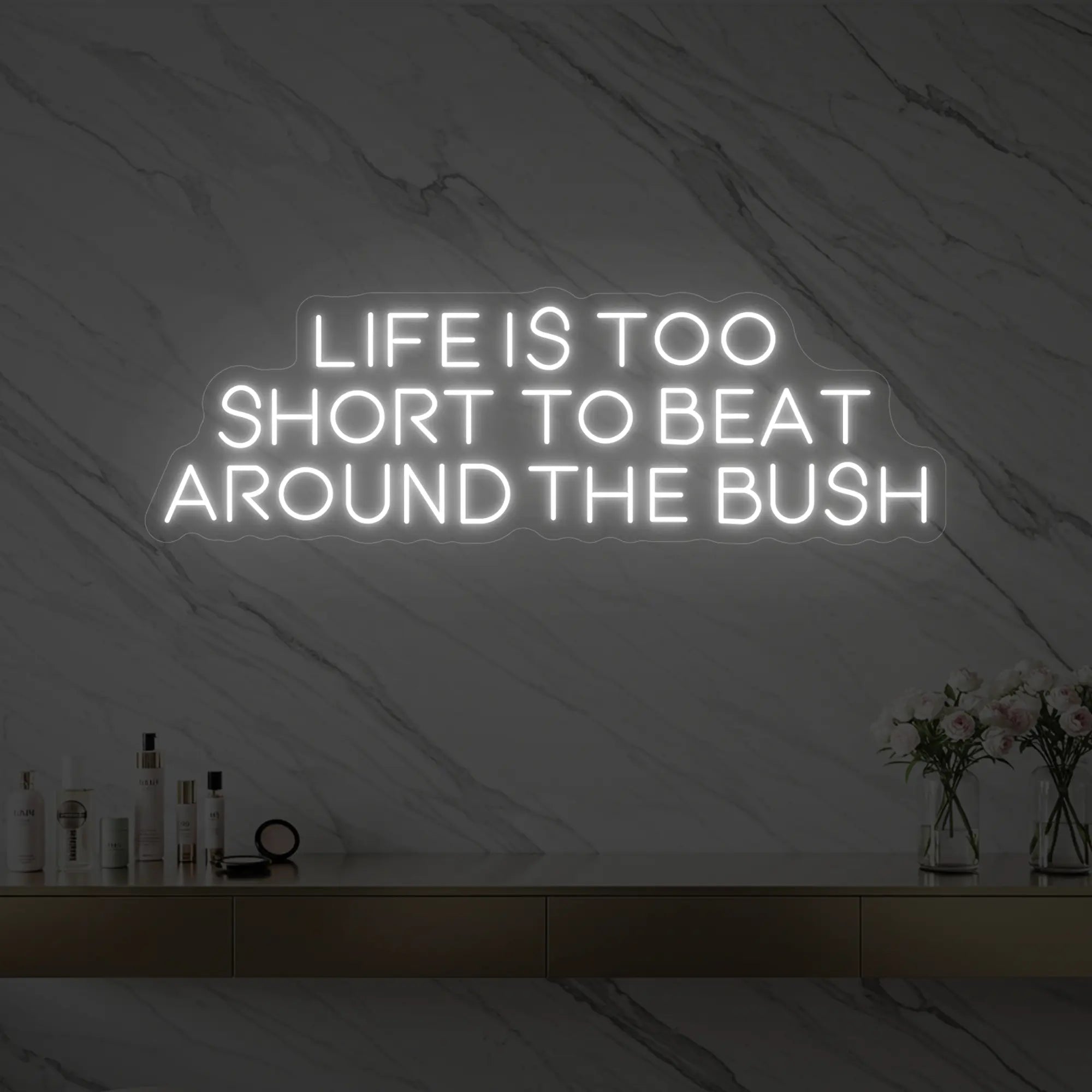 Photo of the 'Life is too short to beat around the bush' neon sign glowing in cool white against a marble wall.