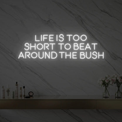 Photo of the 'Life is too short to beat around the bush' neon sign glowing in cool white against a marble wall.