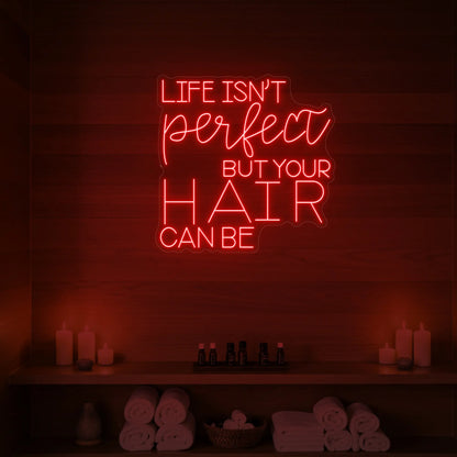 Photo of the 'Life isn’t perfect but your hair can be' neon sign glowing in red against a wood-paneled spa wall.