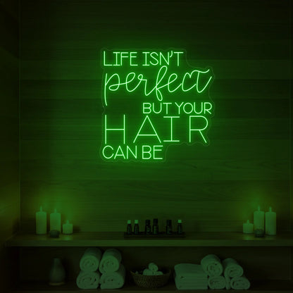 Photo of the 'Life isn’t perfect but your hair can be' neon sign glowing in green against a wood-paneled spa wall.