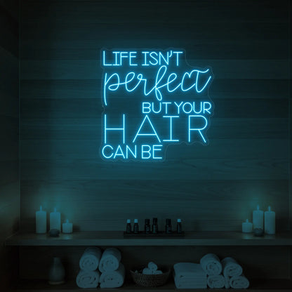 Photo of the 'Life isn’t perfect but your hair can be' neon sign glowing in ice blue against a wood-paneled spa wall.