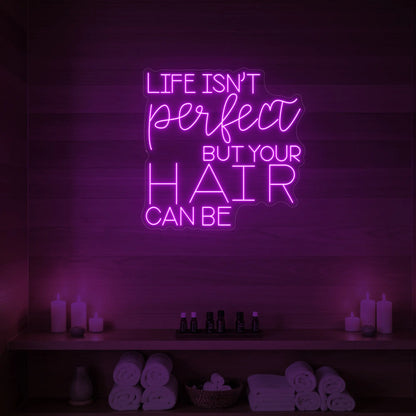 Photo of the 'Life isn’t perfect but your hair can be' neon sign glowing in deep pink against a wood-paneled spa wall.