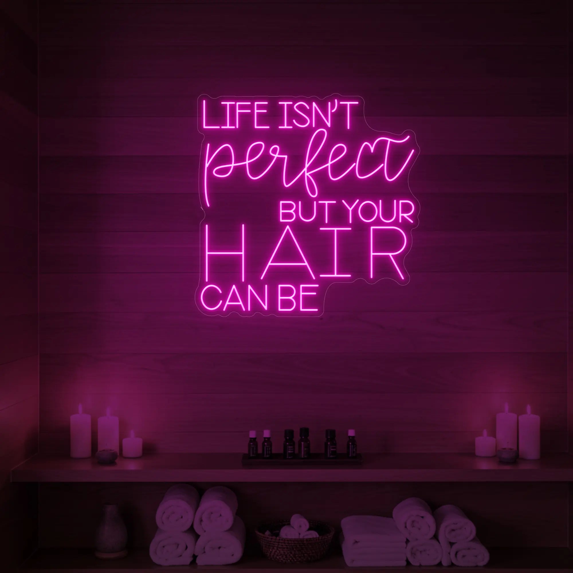 Photo of the 'Life isn’t perfect but your hair can be' neon sign glowing in light pink against a wood-paneled spa wall.