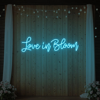 Photo of the 'Love in Bloom' neon sign glowing in ice blue against a styled interior wall.