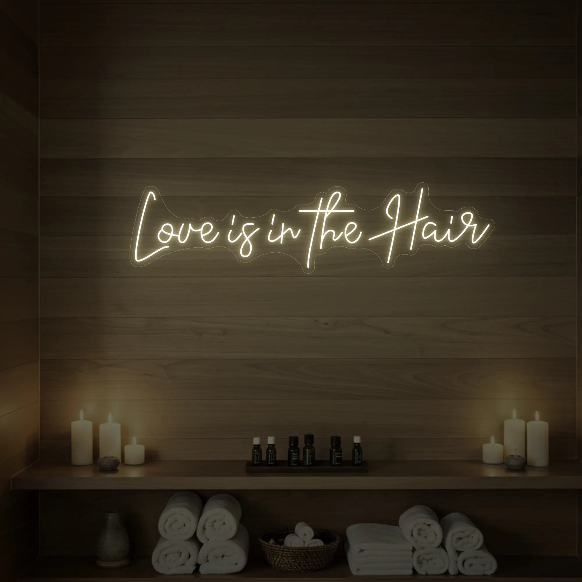Photo of the 'Love is in the Hair' neon sign glowing in warm white against a styled interior wall.