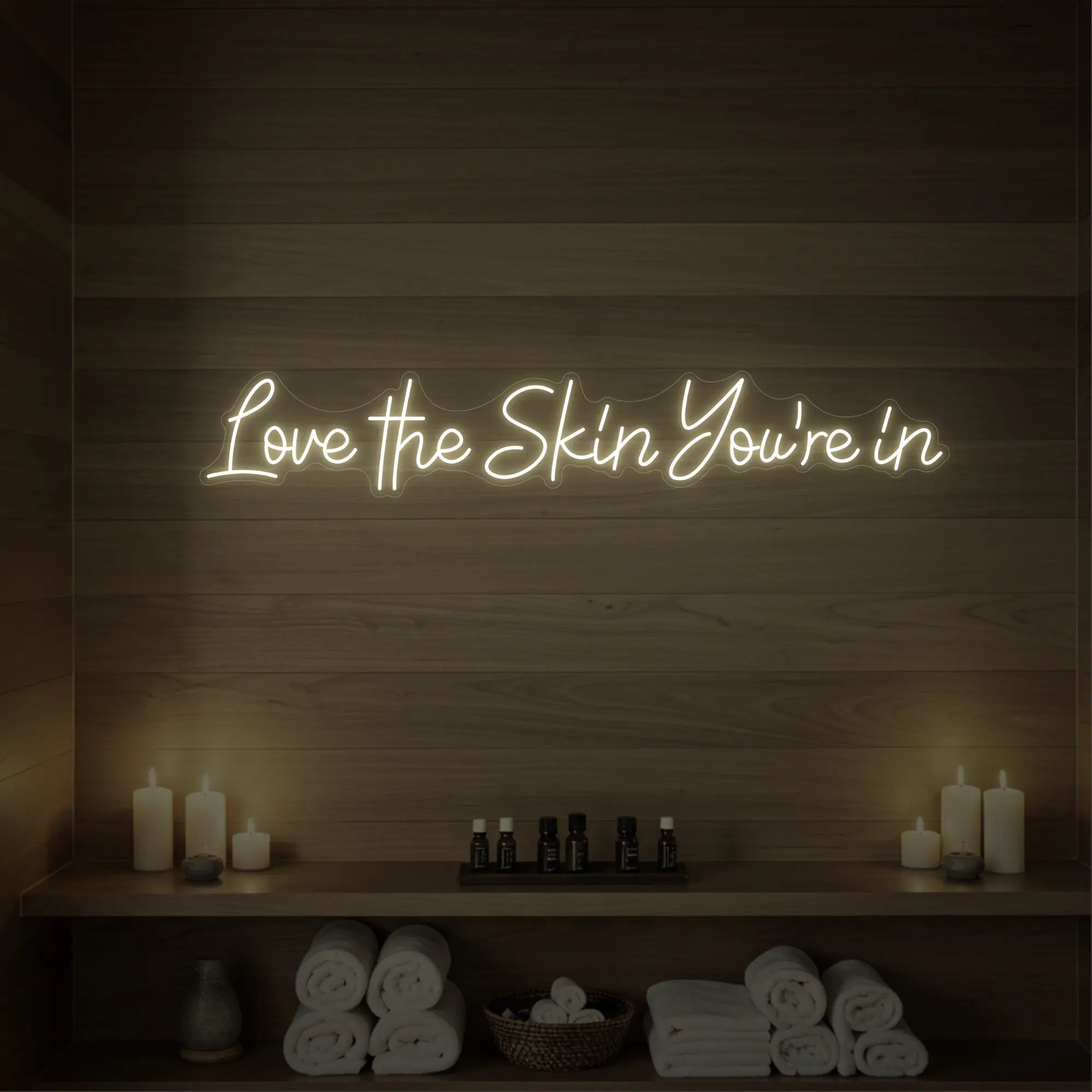 Photo of the 'Love the Skin You're In' neon sign glowing in warm white against a styled interior wall.